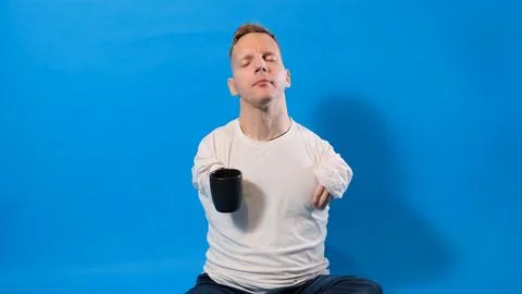 A man with disabilities drinks tea from a cup on a blue isolated background. Stock Photos