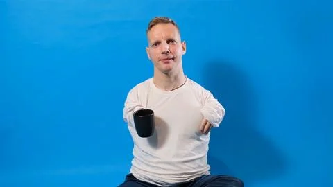 A man with disabilities drinks tea from a cup on a blue isolated background. Stock Photos