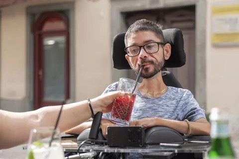 Man with disability enjoys drink while dining with personal assistant Stock Photos