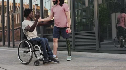 Man with disability leg prosthesis greeting friend on wheelchair outdoor   Stock Footage 197325139