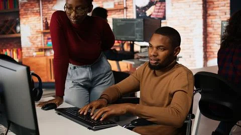 Man with disability typing on PC and chatting with coworker Stock Photos