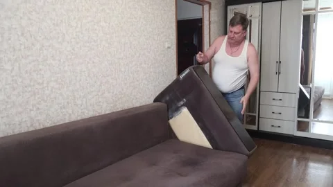 A man disassembles a sofa, removes the side backs for bedbug treatment 動画素材 289442825