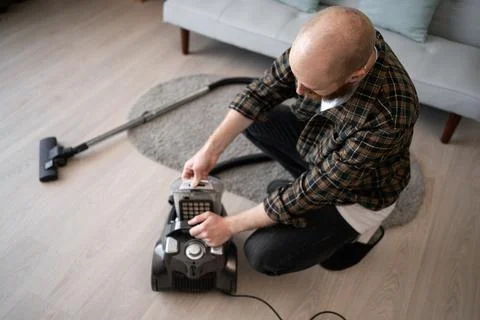 Man disassembles vacuum cleaner after cleaning takes out container with dirt  Stock Photos