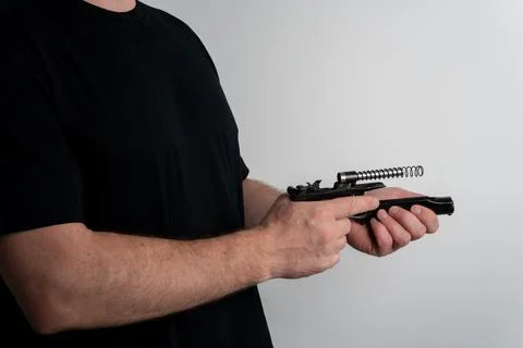 Man disassembling semi automatic pistol for maintenance on plain background Fotos Stock