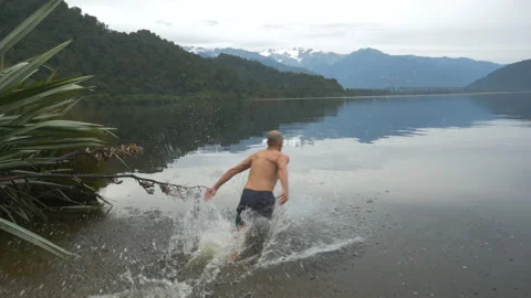 A man dives into a lake with mountains around, in New Zealand Stock Footage 219926392