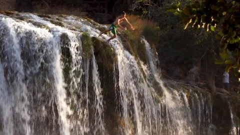Man diving acrobatic jumping in water from the rock cliffs of a wild waterfall Stock Footage 90267571