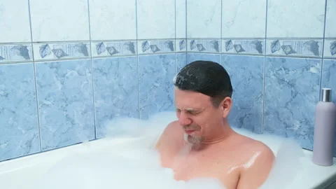 Man is diving in bathroom sitting in bath with foam relaxing at home. Stock Footage 158383998