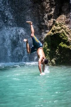 Man diving headfirst into a turquoise pool beneath a waterfall. Stock Photos