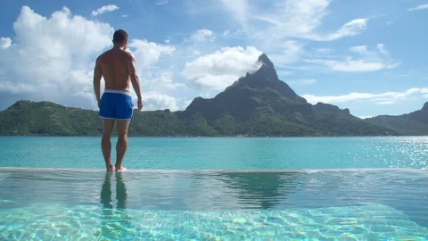 A man diving in a pool, lifestyle in a pool on Bora Bora with Mount Otemanu at a Stock Footage 102579327