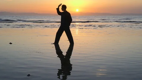 Man do energy practices at mirrored surface of sunset shallow water Stock Footage 126000320