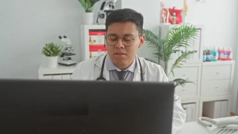 Man doctor looks at computer screen with stethoscope on white coat in clini.. Video stock 337354802