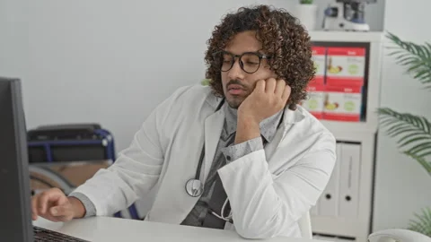 Man doctor with stethoscope at computer resting hand on cheek at desk in a .. Stock Footage 337405805