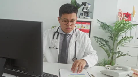Man doctor in white coat flips report pages at desk beside computer and tel.. Stock Footage 337354853