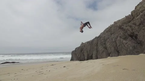 Man Does a Backflip off of Rocks on Beach in Slow Motion Stock Footage 50000112