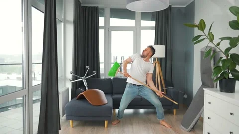 Man does the cleaning and imagines himself a rock star, plays the broom like a Video stock 165178208