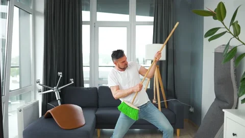Man does the cleaning and imagines himself a rock star, plays the broom like a Stock Footage 171547919