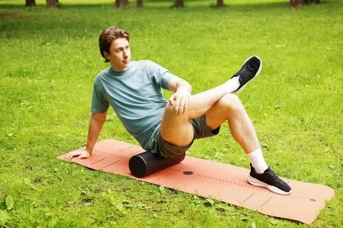 Man does foam rolling on a park mat for myofascial release and self-massage.. Stock Photos