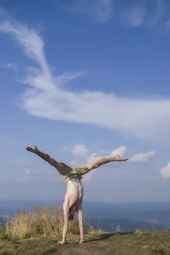 A man does a handstand on top of a mountain in the summer 写真素材