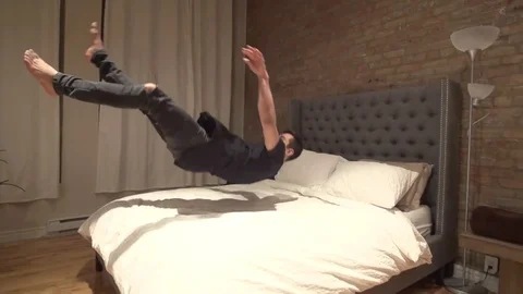 Man Does Jump and Lands on White Bed Sheets Smiling in Slow Motion Stock Footage 82352853