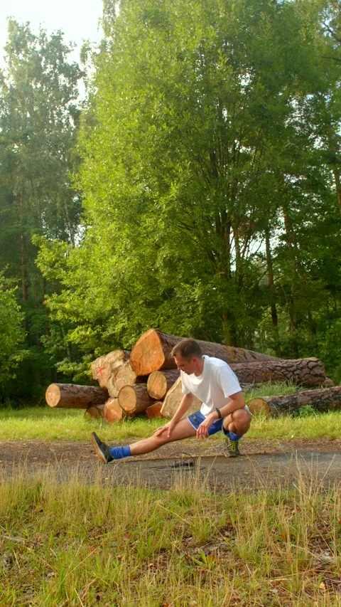 A man does leg stretches and squats outdoors in a serene wood Stock Footage 314346473