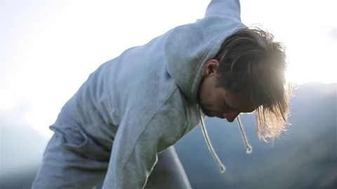 Man does morning exercise cross-touching feet rotating hands warm up outdoors Video stock 79970730