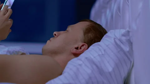 The man does not sleep, he looks at the news on his phone, camera movement Stock Footage 131346425