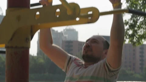 A man does pull-ups on a horizontal bar during an outdoor workout. Stock Footage 157773290