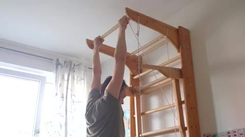 A man does pullups in a sunny room, inspiring a child nearby Stock Footage 311206023