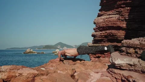 A man does push-ups from the floor on rocks by the sea Stock Footage 235381815