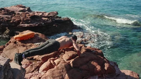 A man does push-ups from the floor on rocks by the sea Stock Footage 235381890