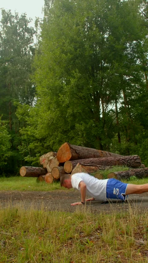 A man does pushups outdoors by a large log pile, showing strength Stock Footage 314345970