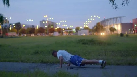 A man does pushups in a park, training day and night, then runs Stock Footage 317340298