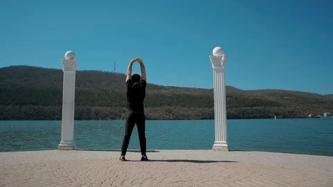 Man does stretching and warming up in a beautiful place on the lake Stock Footage 105970279