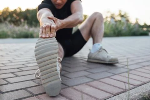 Man does stretching exercises on paving tile in outdoor park Stock Photos