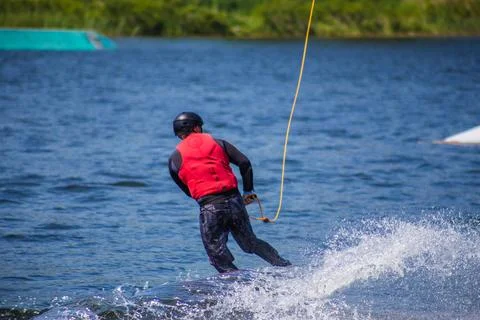 The man does wakeboarding on the water in the summer in a helmet and wetsuit. Stock Photos