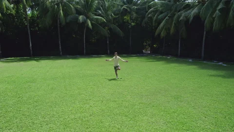 Man does yoga on the lawn against the background of palm trees Stock Footage 243296525