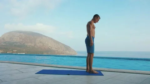 Man does yoga by the pool, with sea and mountain views Stock Footage 131460412