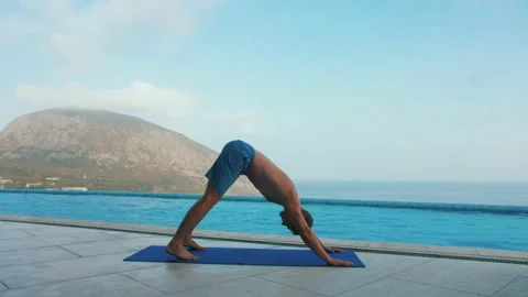 Man does yoga by the pool, with sea and mountain views Stock Footage 131460712