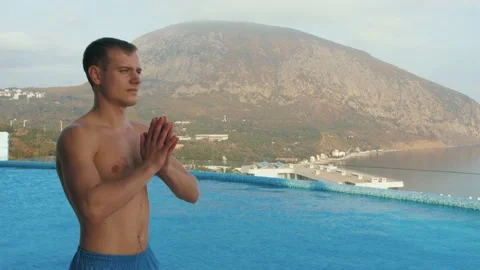 Man does yoga by the pool, with sea and mountain views Stock Footage 131460984