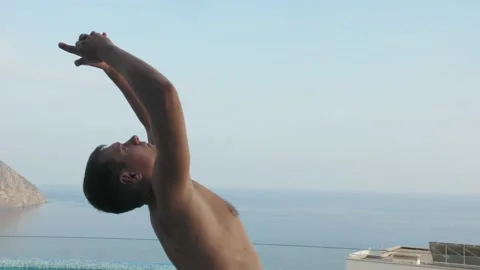 Man does yoga by the pool, with sea and mountain views Stock Footage 131461375