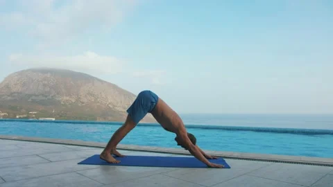 Man does yoga by the pool, with sea and mountain views Stock Footage 131464129