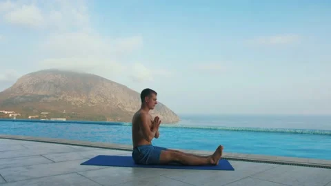 Man does yoga by the pool, with sea and mountain views Stock Footage 131464709