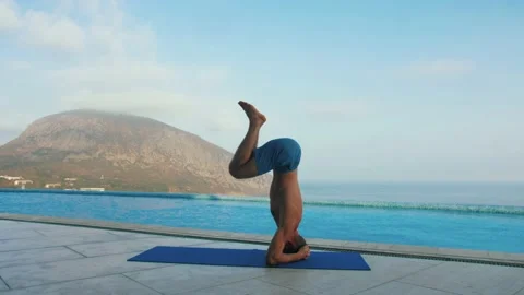 Man does yoga by the pool, with sea and mountain views Stock Footage 131464895