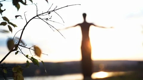 A man does yoga on the river bank at sunset. The image looks like an alien. Stock Footage 149556917