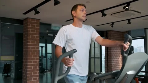 Man doing cardio training on elliptical machine in modern fitness studio in Stock Footage 280942316