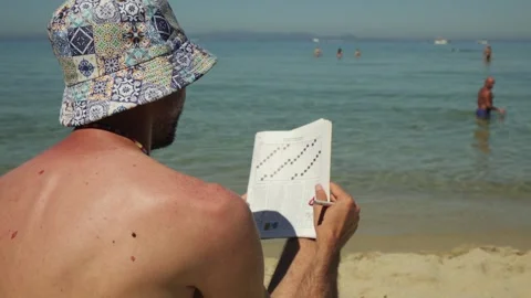 Man doing crossword puzzle on beach, Elba island, Italy 動画素材 336315309