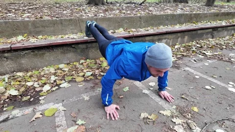 Man doing decline push ups with feet on bench in autumn park, training chest Stock Footage 318171766