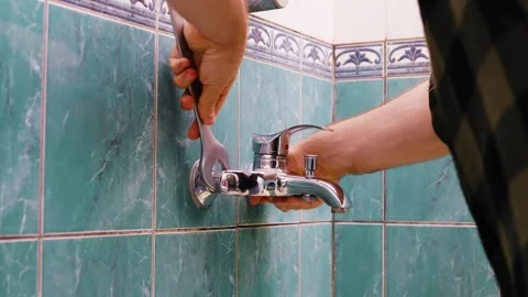 Man doing DIY plumbing repairs, using a wrench to replace an old faucet on a gre Stock Footage 337493455