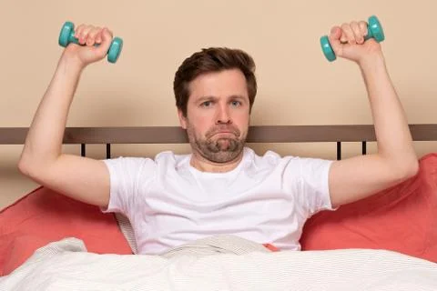 Man doing dumbbell front raises while exercising at home resting at bed durin Stock Photos