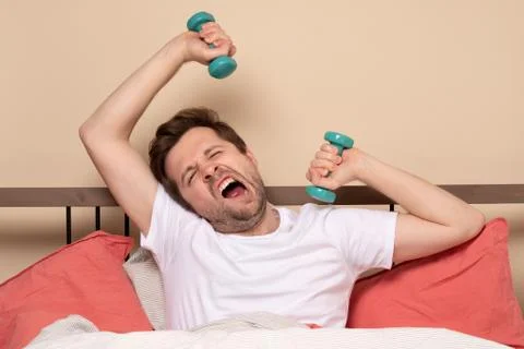 Man doing dumbbell front raises while exercising at home resting at bed durin Stock Photos